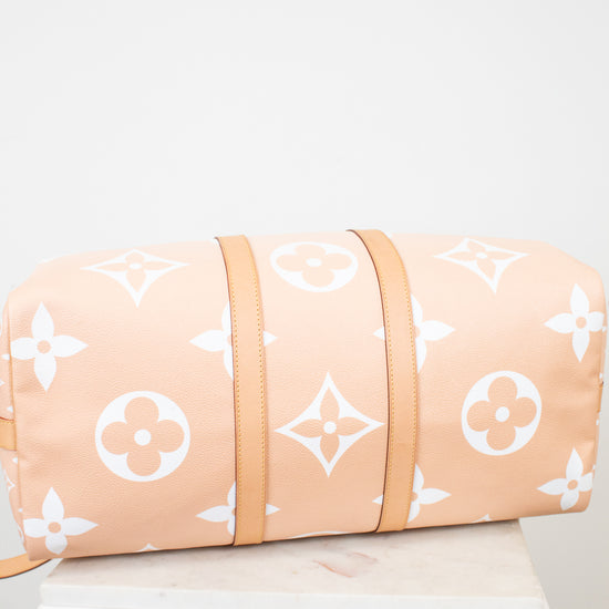 Bottom view of beige duffle bag with white monogram pattern on a light gray background