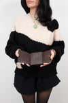 Person wearing a black and white sweater holding a brown wallet open against a plain background