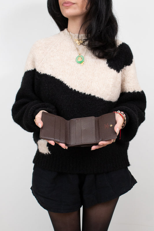Person wearing a black and white sweater holding a brown wallet open against a plain background