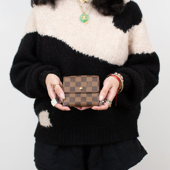 Person wearing a black and white sweater holding a brown checkered wallet against a plain background