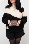 Person wearing a black and white sweater holding a brown checkered wallet against a plain background