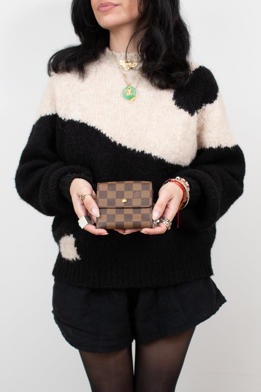 Person wearing a black and white sweater holding a brown checkered wallet against a plain background