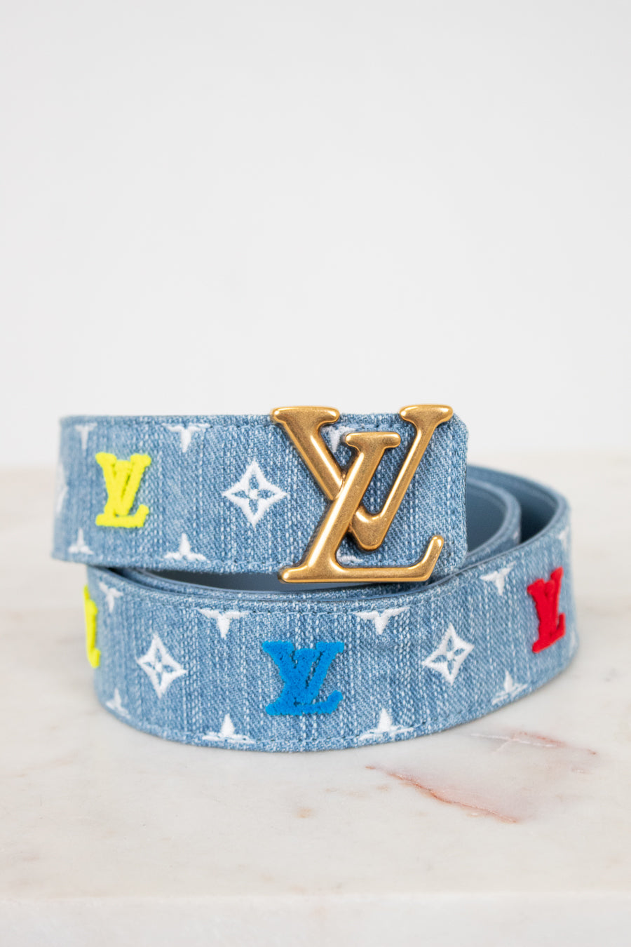 Louis Vuitton denim belt with gold buckle and mixed color monogram on white background