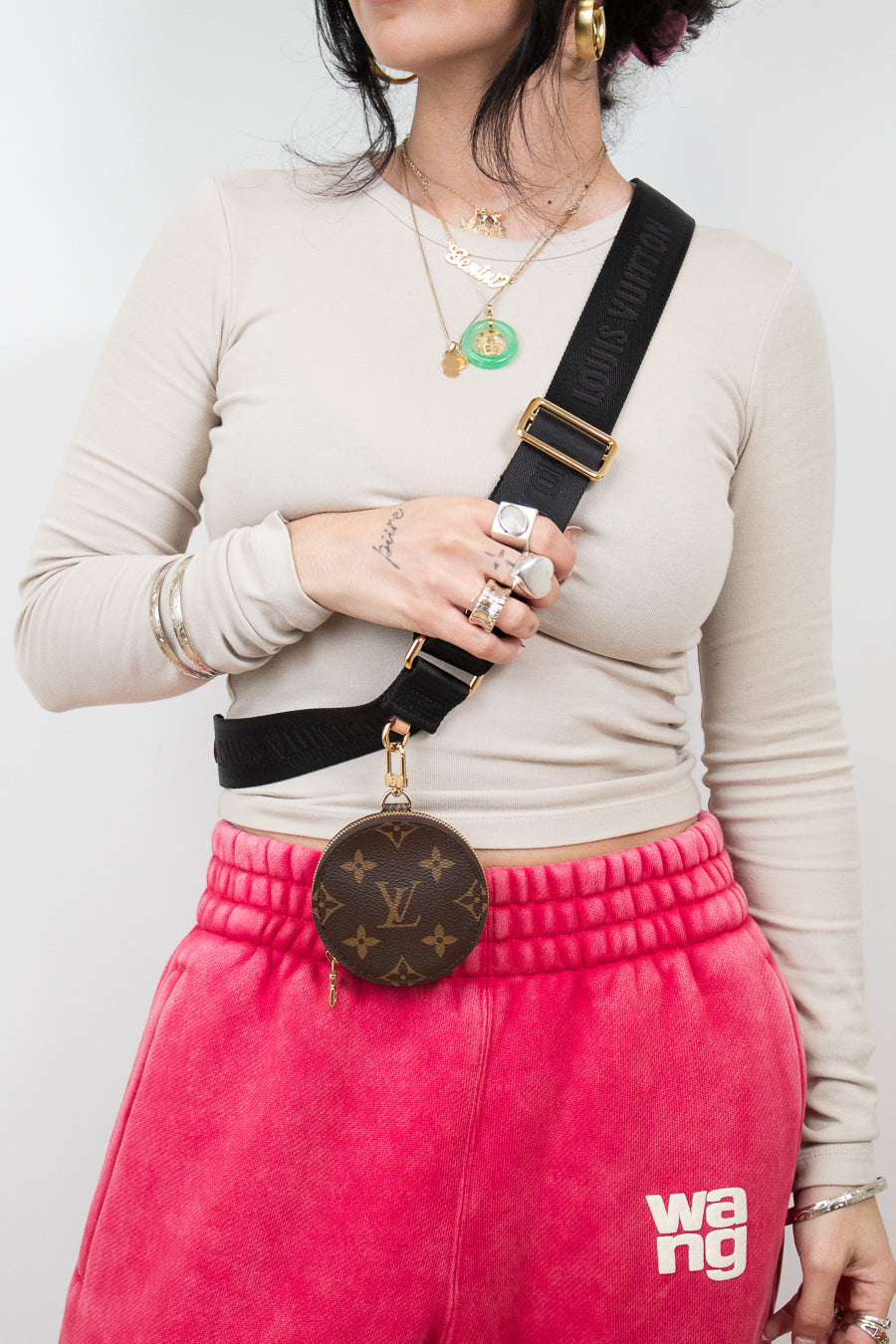 Person wearing a beige long-sleeve top, pink sweatpants with 'Wang' branding, and carrying a Louis Vuitton bag.