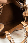 Close-up of a brown leather handbag with chain details on a light wooden surface.