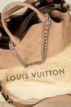 Louis Vuitton handbag with monogram pattern and chain detail on a beige surface.