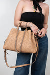 Person holding a tan handbag with a chain detail against a plain background