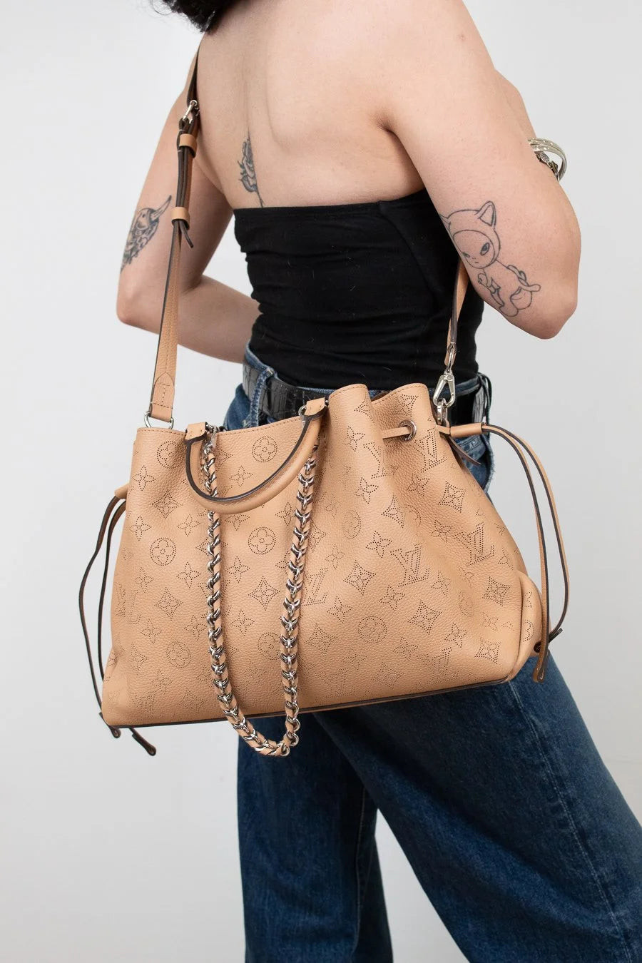 Person holding a beige handbag with a chain detail against a plain background