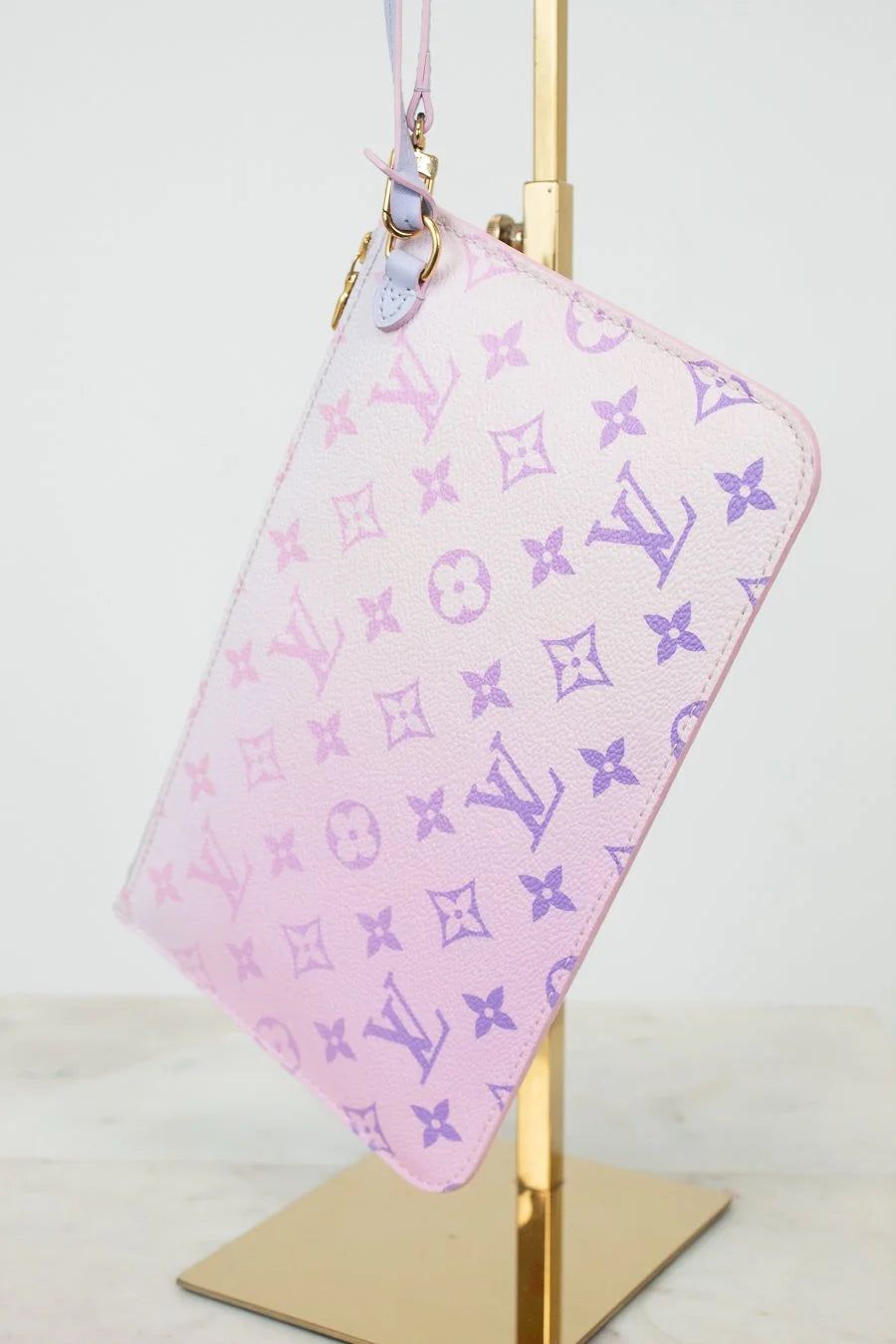 Ombre Pink pouch with purple monogram pattern on a gold stand against a white background