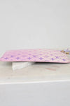 Pink pouch with a purple monogram brand logo on a white surface