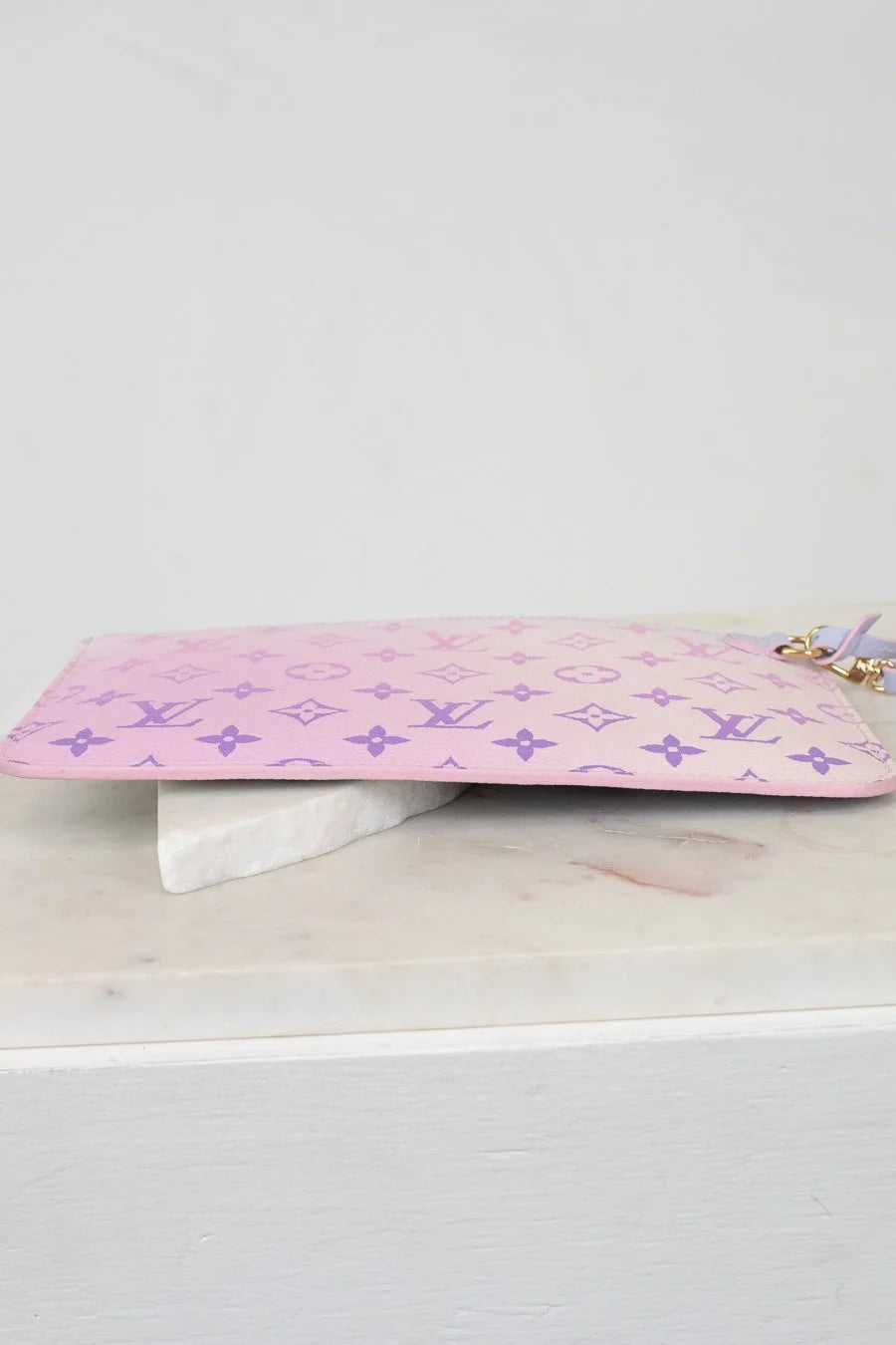 Pink pouch with a purple monogram brand logo on a white surface