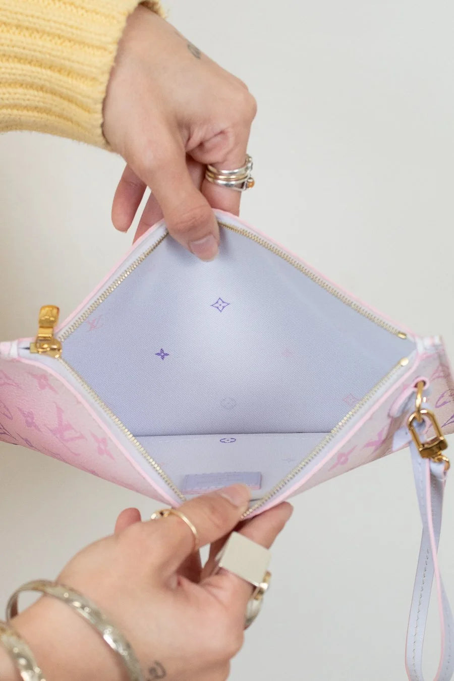 Close-up of a hand holding an open pink wallet with blue interior and gold accents on a light background