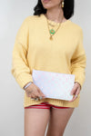 Person wearing a yellow sweater holding a ombre pink to blue clutch with pink patterns against a plain background