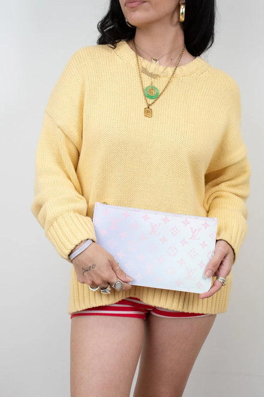Person wearing a yellow sweater holding a ombre pink to blue clutch with pink patterns against a plain background