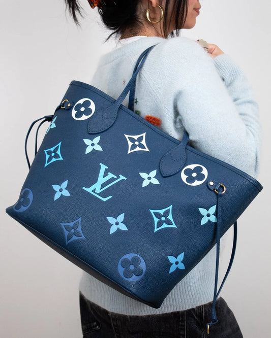 Person carrying a blue handbag with brand logo patterns on a plain background