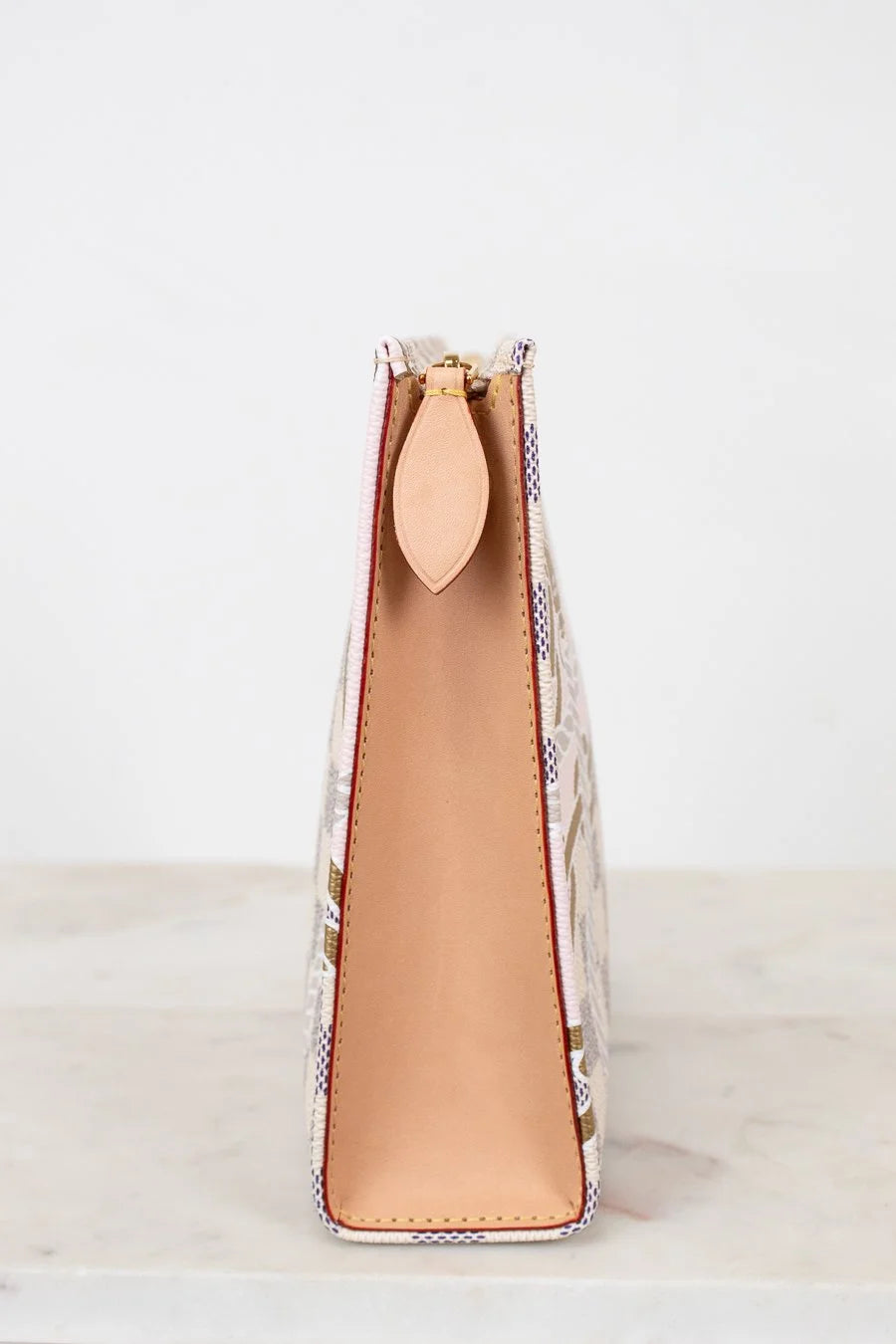 Close-up of side profile of clutch/pouch with a patterned front and beige interior on a light background