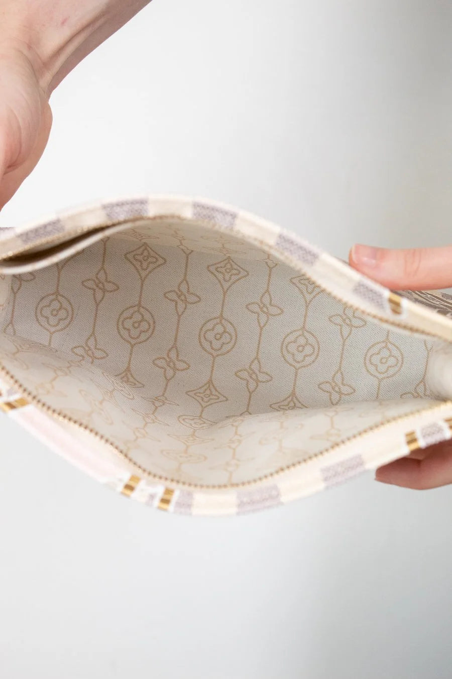 Close-up of a hand holding an open pouch with floral logo patterns on a light gray background
