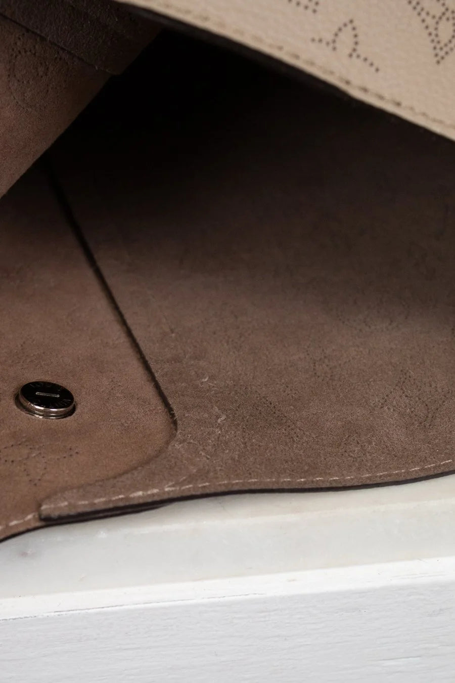 Close-up of a brown leather product with a button on a white surface