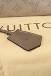 Beige leather exterior tag on a beige surface with Louis Vuitton branding. Showing black marks to leather tag
