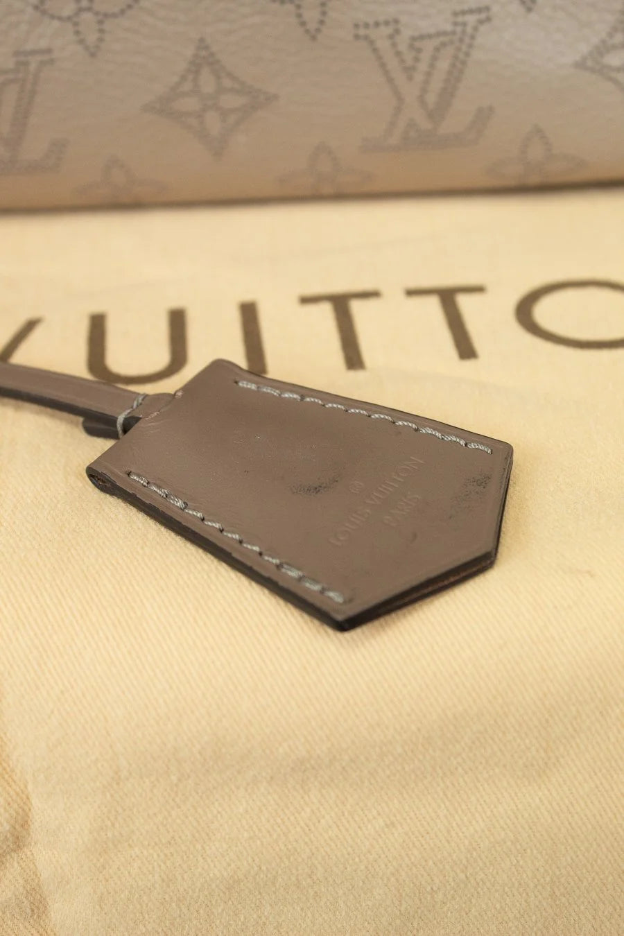 Beige leather exterior tag on a beige surface with Louis Vuitton branding. Showing black marks to leather tag