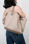 Person wearing a beige monogram handbag on a plain background