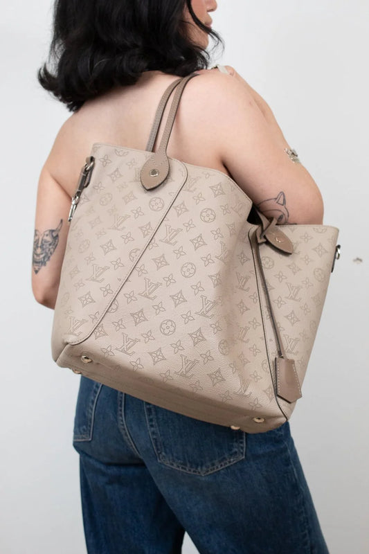 Person wearing a beige monogram handbag on a plain background