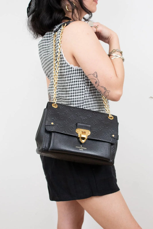 Person holding a black handbag with gold accents against a white background