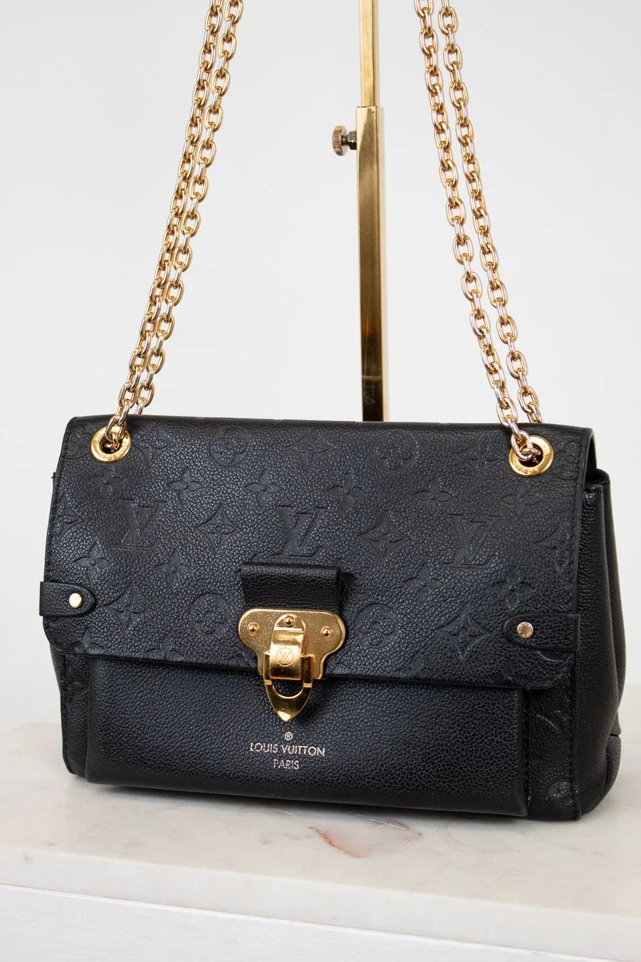Black handbag with gold chain and clasp on a white surface