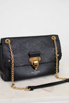 Black handbag with gold chain and clasp on a white surface