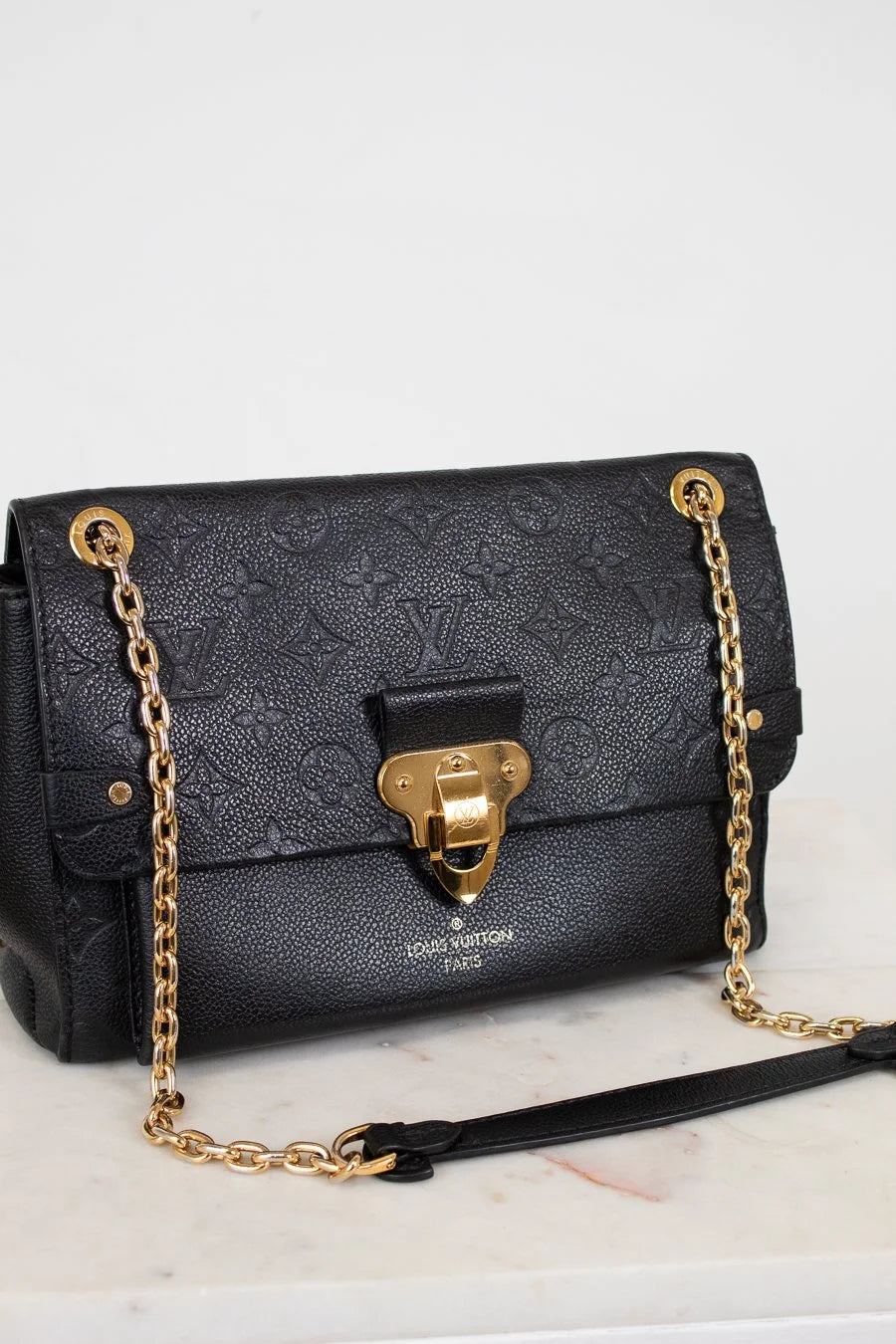 Black handbag with gold chain and clasp on a white surface