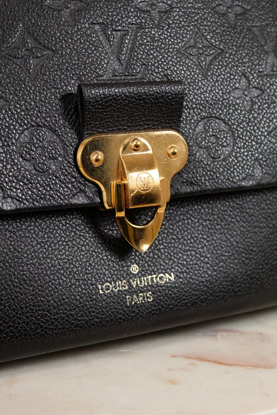 Black Louis Vuitton handbag with gold clasp on a marble surface