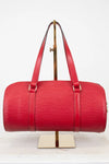 Red handbag on a gold stand against a white background