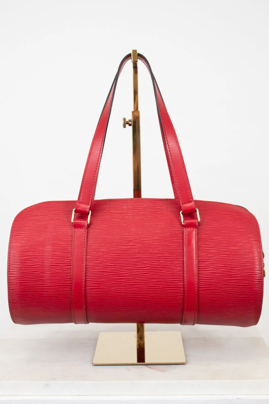 Red handbag on a gold stand against a white background