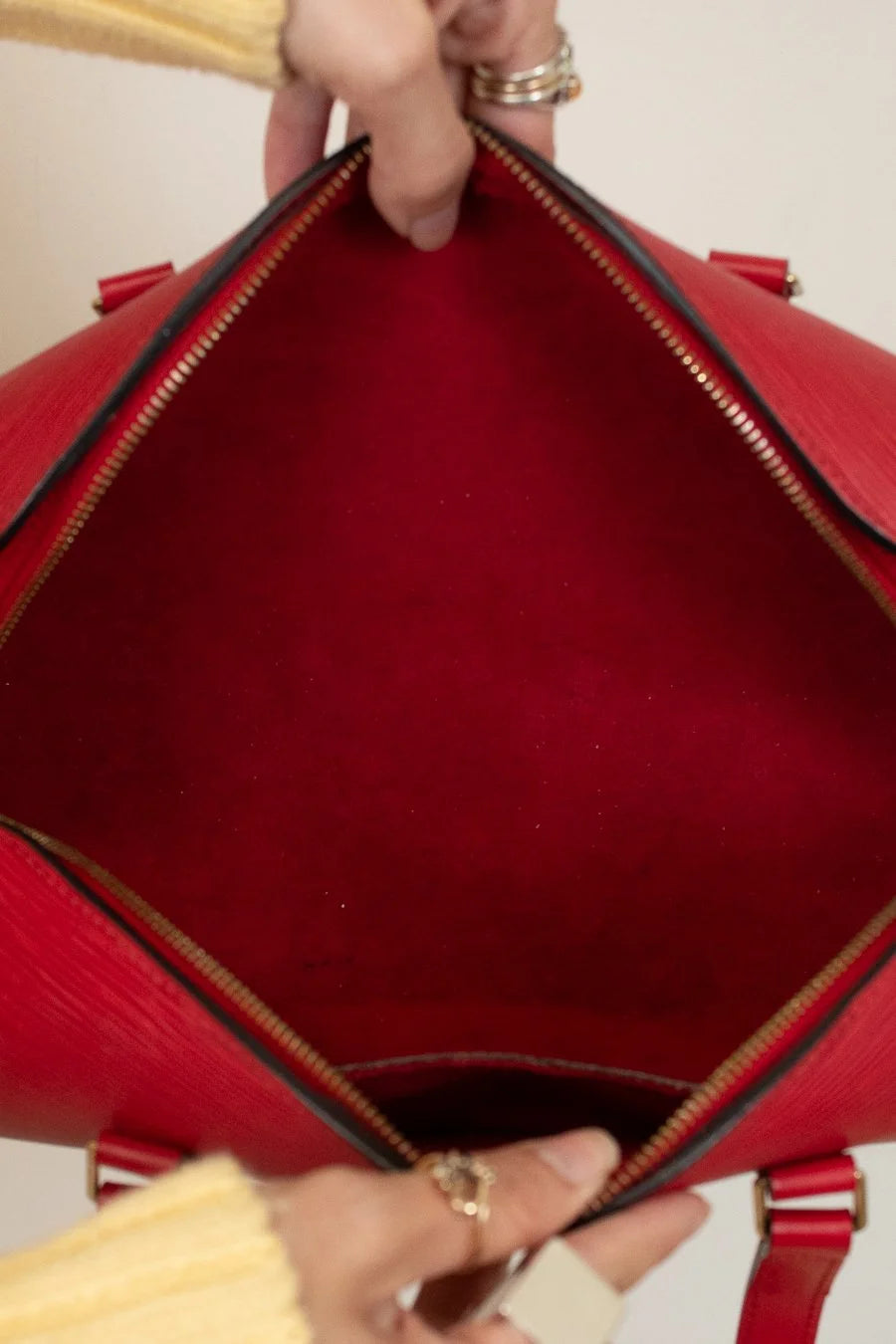Red handbag held open by a person's hands, showing the interior.