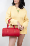 Person wearing a yellow sweater holding a red handbag against a plain background