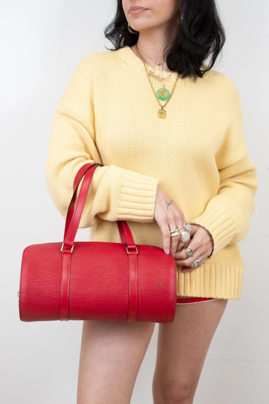Person wearing a yellow sweater holding a red handbag against a plain background