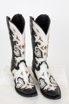 A pair of western cowboy boots with a black and white leather design, featuring intricate brown and black embroidery and silver-tone studs, displayed on a white marble surface against a white background.