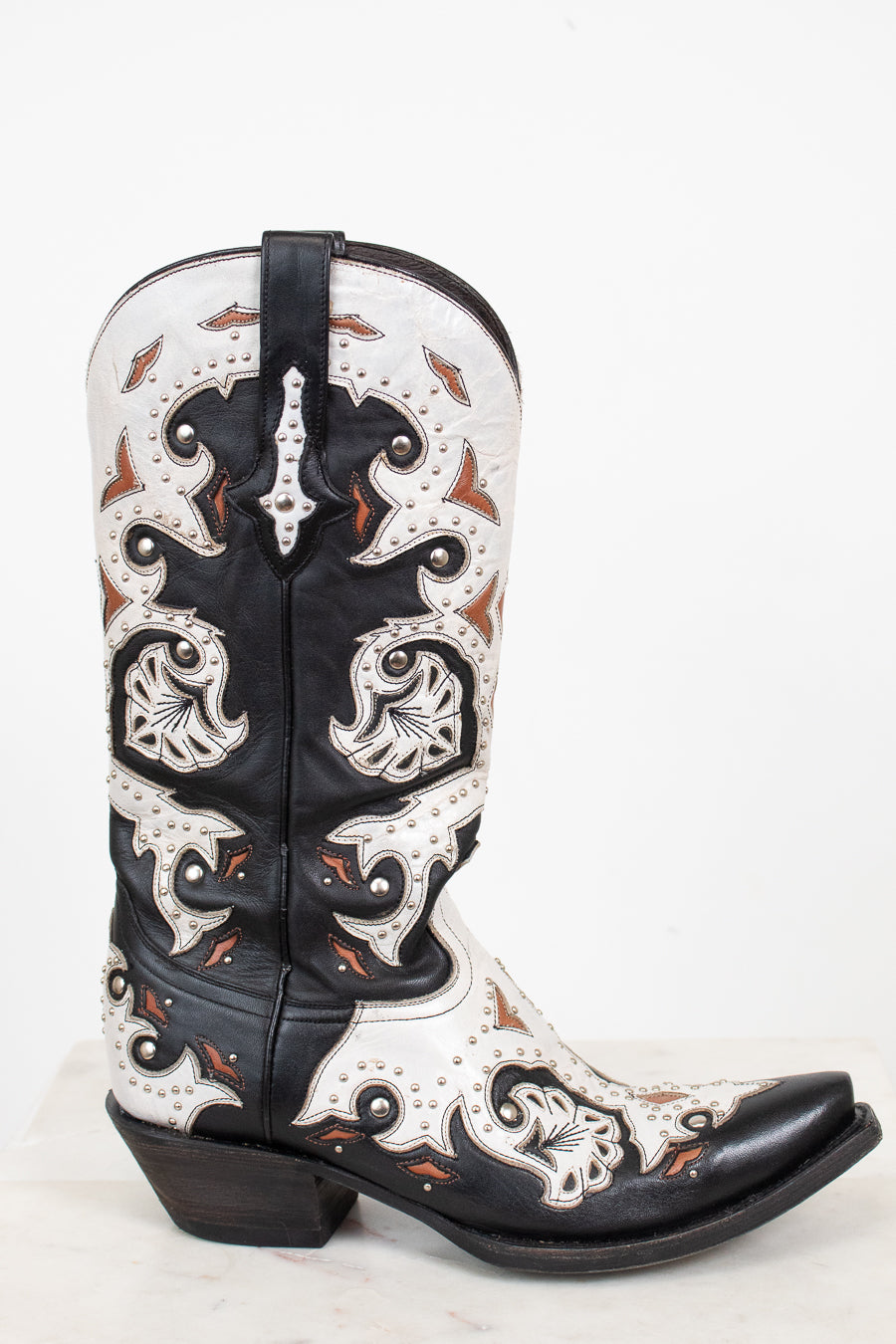 A single western cowboy boot with a black and white leather base, featuring intricate orange-brown accents, and silver studded detail, set against a plain white background.