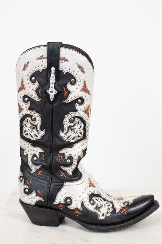 A single western cowboy boot with a black and white leather base, featuring intricate orange-brown accents, and silver studded detail, set against a plain white background.