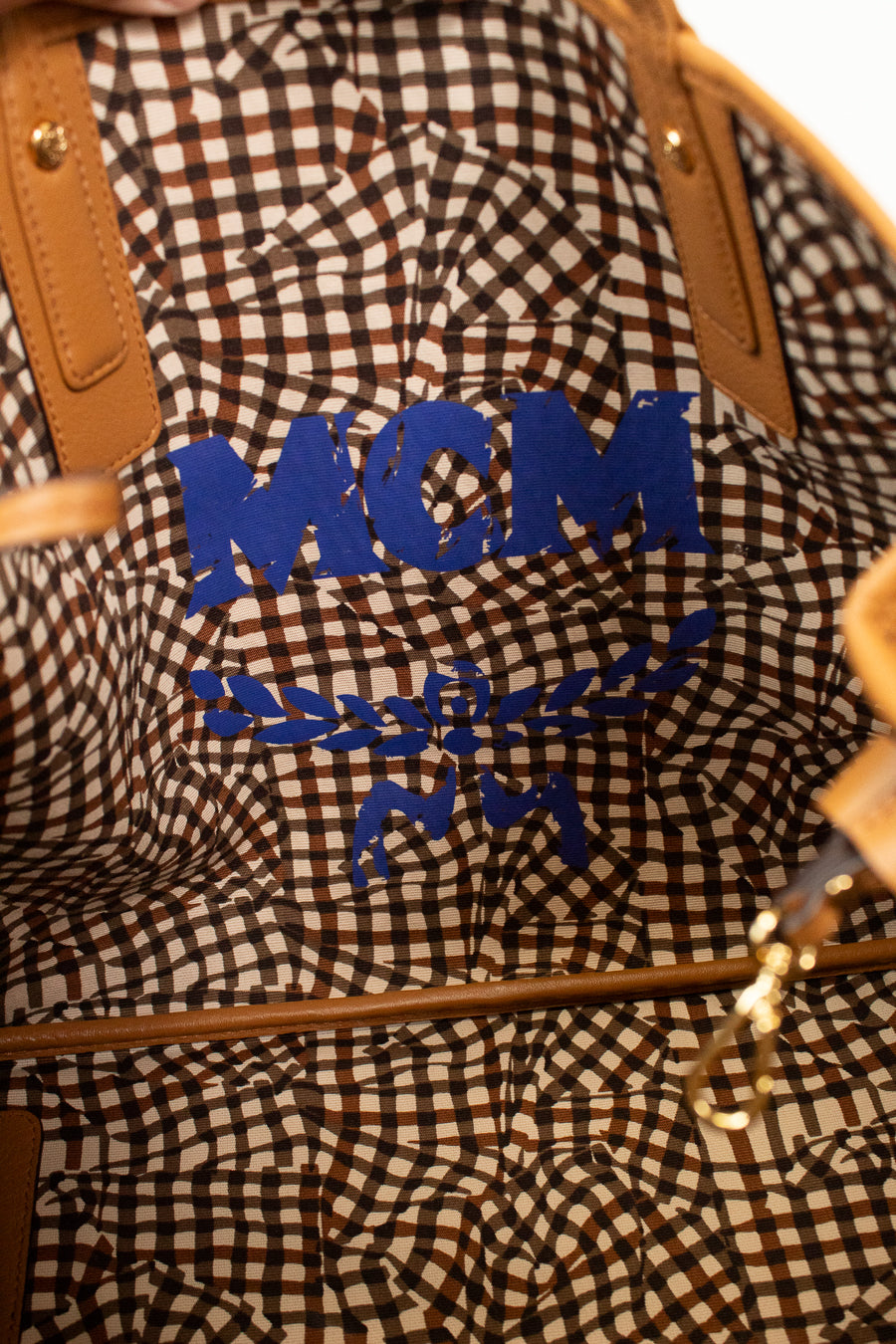 Close-up of an abstract checkered design on bag with 'MCM' branding in blue text.