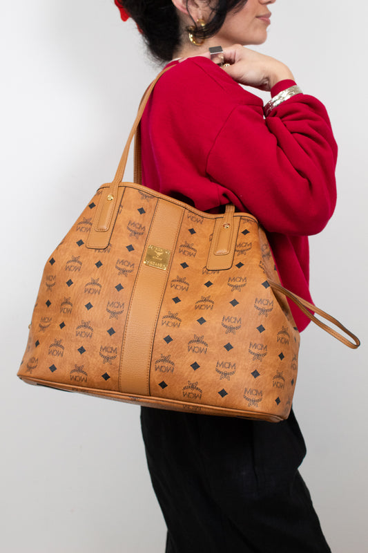 Person holding a brown patterned handbag against a plain background