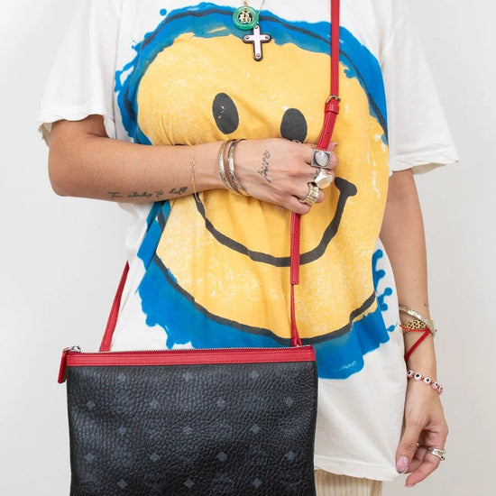 Person wearing a white t-shirt with a smiley face design, holding a black handbag with red straps.
