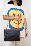 Person wearing a white t-shirt with a smiley face design, holding a black handbag with red straps.
