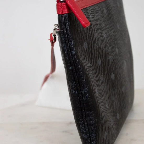 Black textured clutch bag with a red zipper on a white background