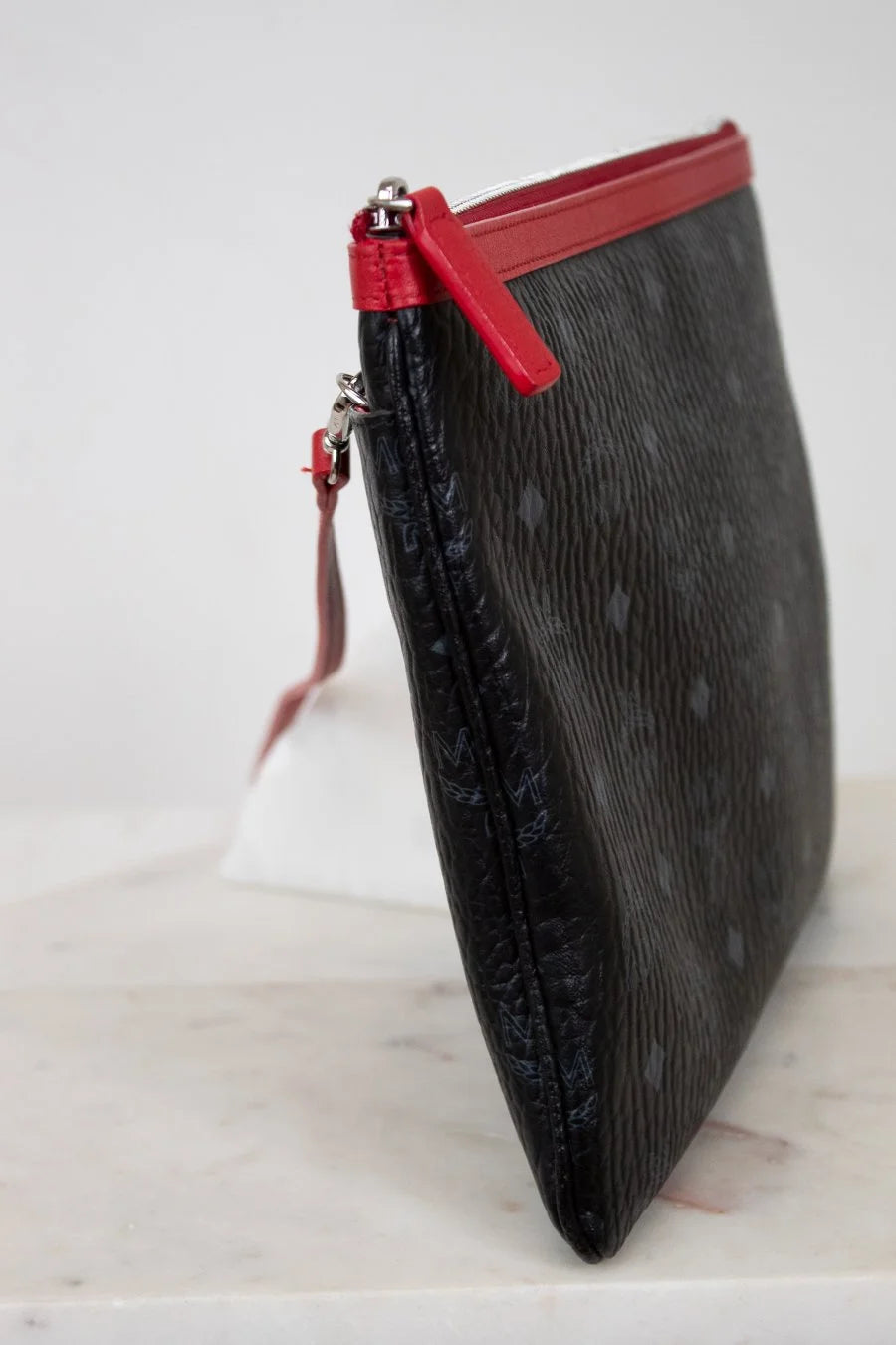 Black textured clutch bag with a red zipper on a white background