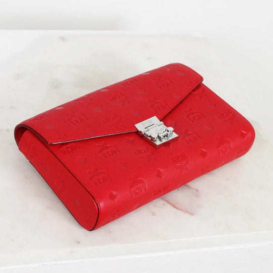 Red embossed clutch bag with a silver clasp on a light wooden surface