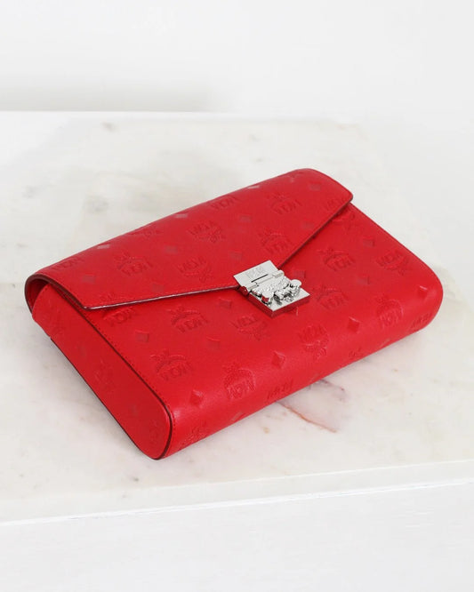 Red embossed clutch bag with a silver clasp on a light wooden surface