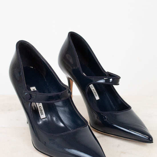 Pair of navy high-heeled shoes with a strap on a light background