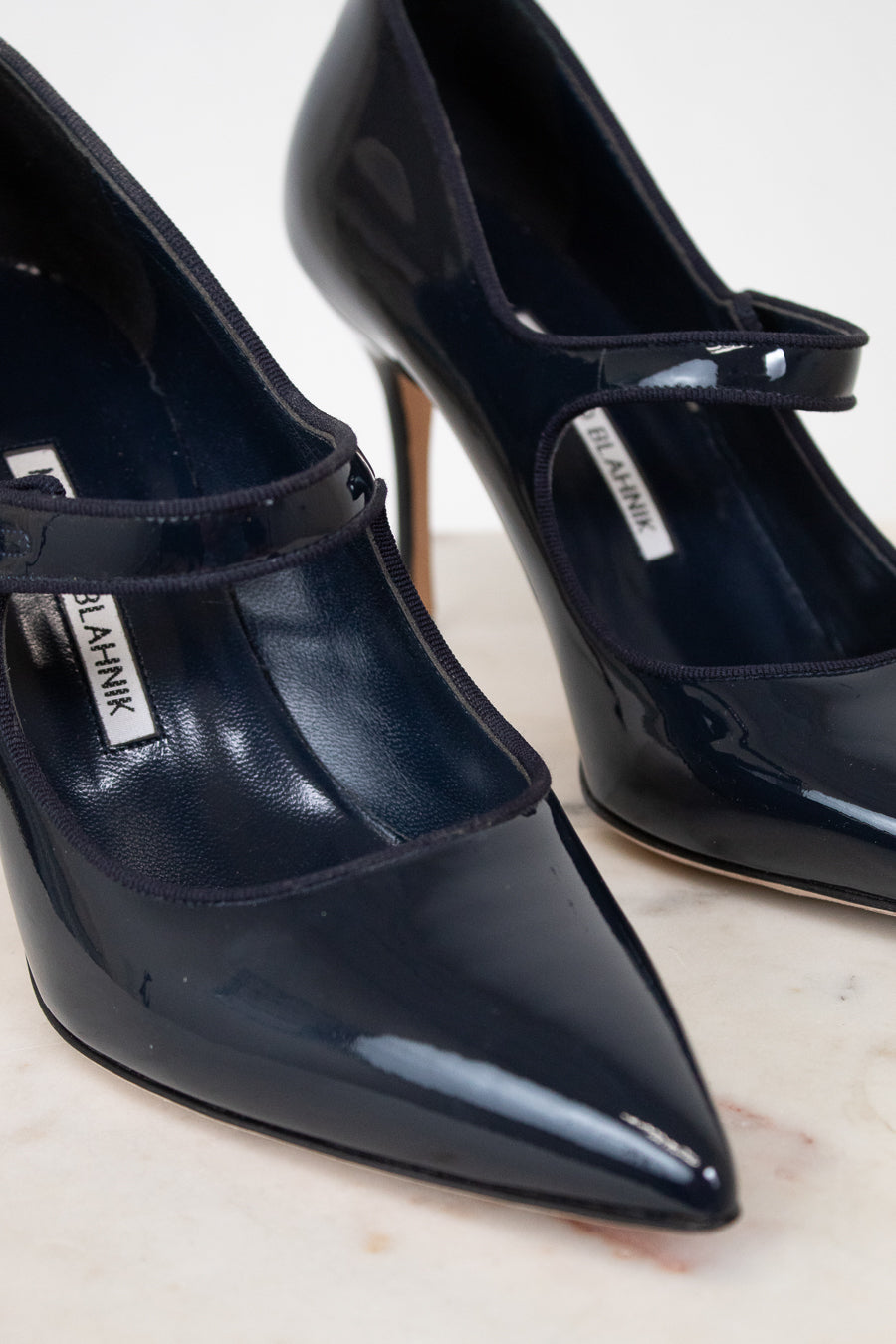 Navy patent high-heeled shoes with a brand label on a light background
