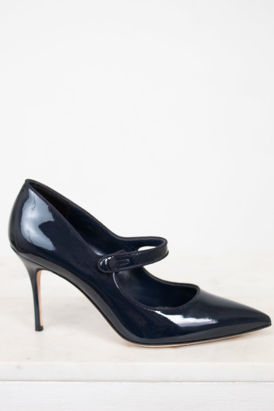 Navy blue patent leather high-heeled shoe with a strap on a white background
